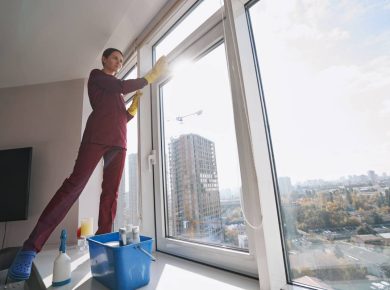 Low angle of dreamy cleaner in uniform standing on windowsill during window cleaning