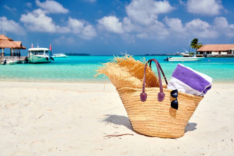 Straw bag with hat and towel on beach. Summer vacation at Maldives.
